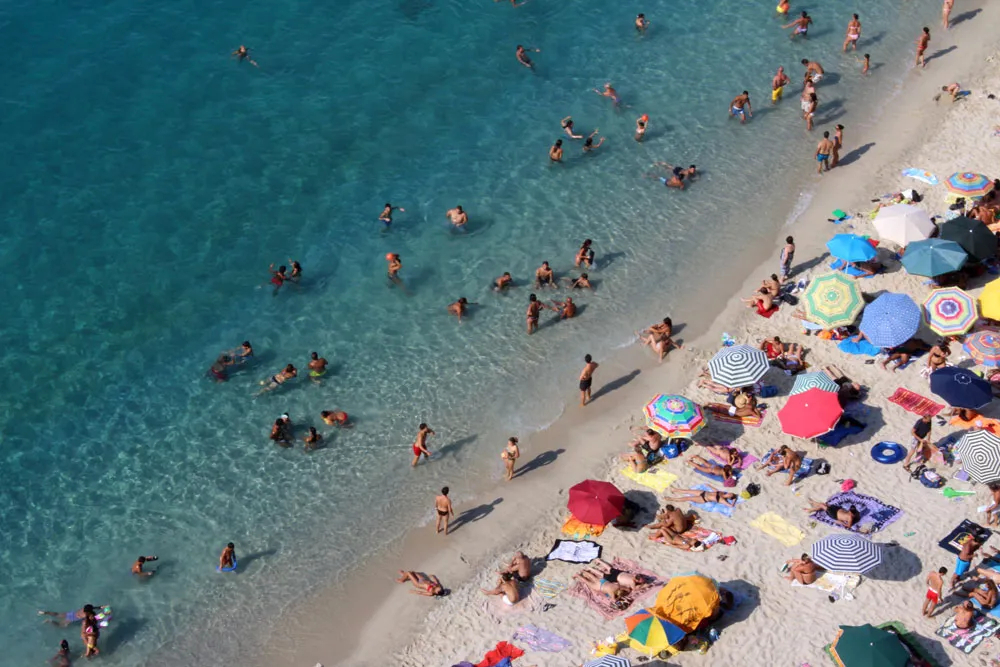 A crowded beach filled with sunbathers, families, and beachgoers enjoying the sunny day by the water